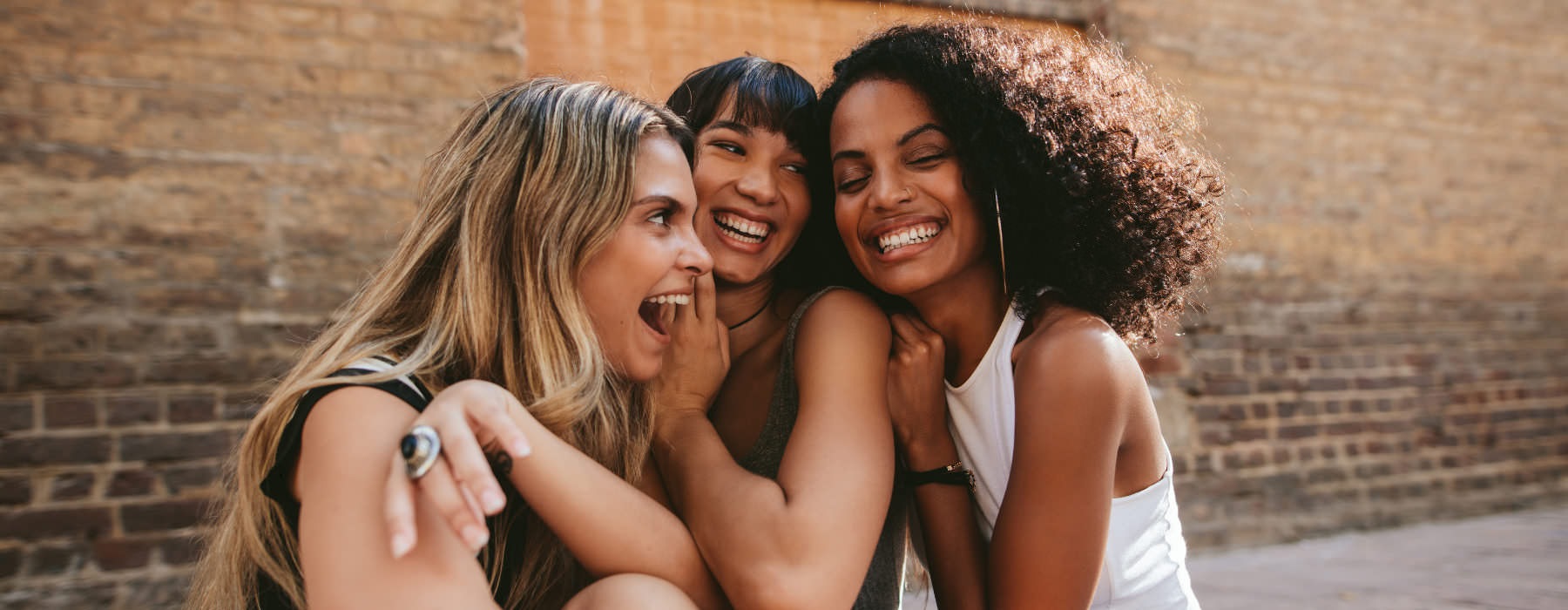 women laugh together on a sidewalk